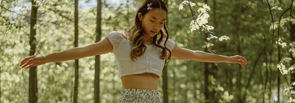 Ein Mädchen mit lockigem Haar und ausgestreckten Armen im sonnigen Wald