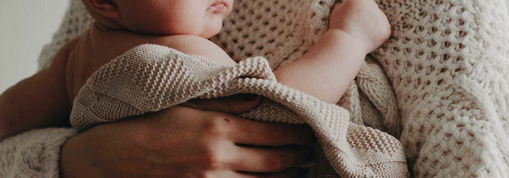 Ein in eine Decke eingewickeltes Baby wird von einer Person eng am Körper gehalten