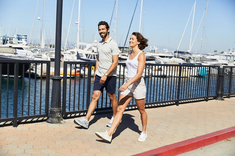 Man and woman wearing DUER outfits walking along a boardwalk