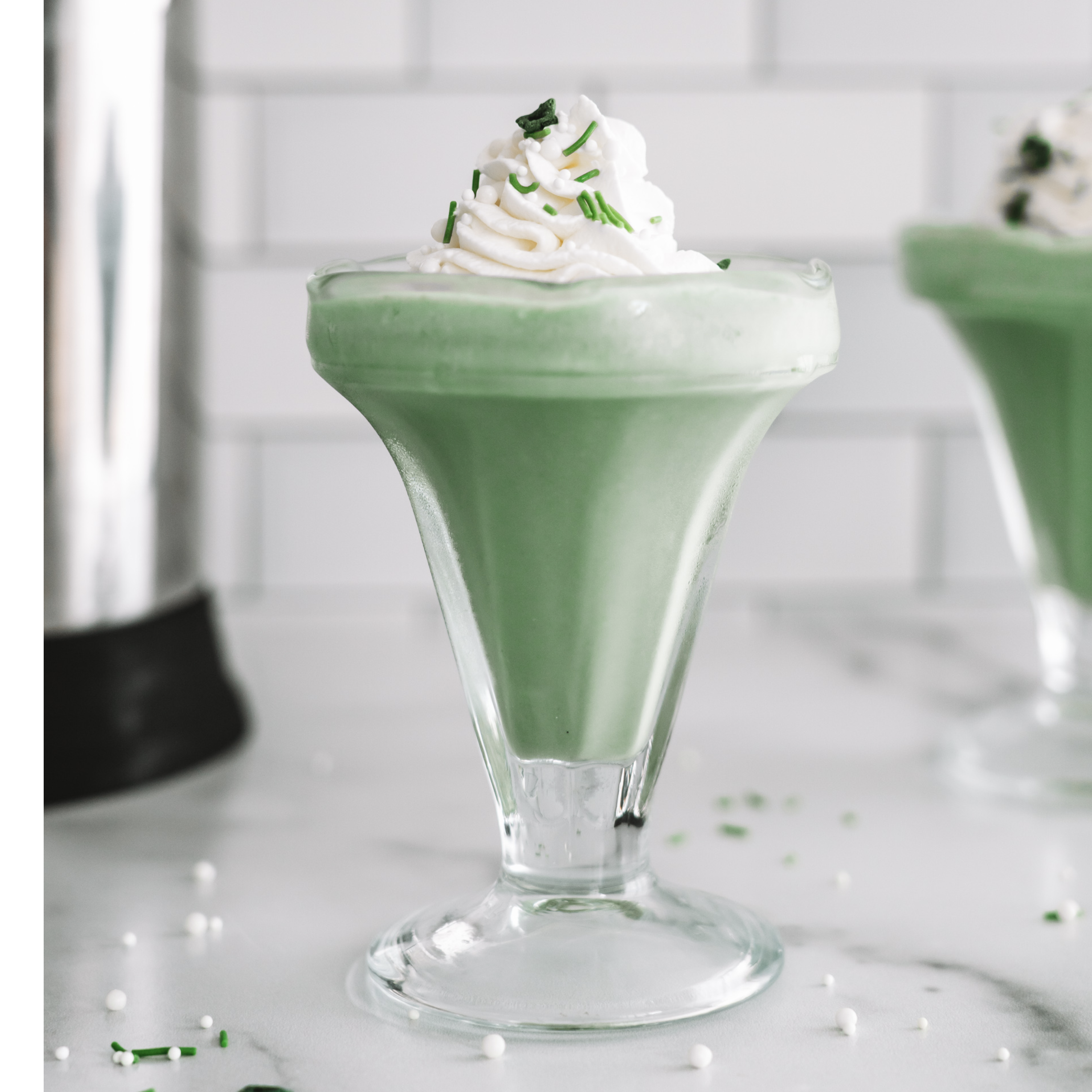 plant-based shamrock shake in a glass garnished with coconut whipped cream and sprinkles