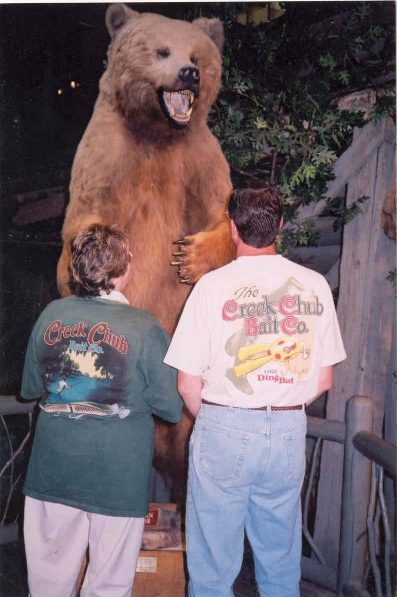 Anita Rolfe & son Ted Thill in front of a large bear display at Bass Pro Shops in their Creek Chub Bait Co. T-shirts.