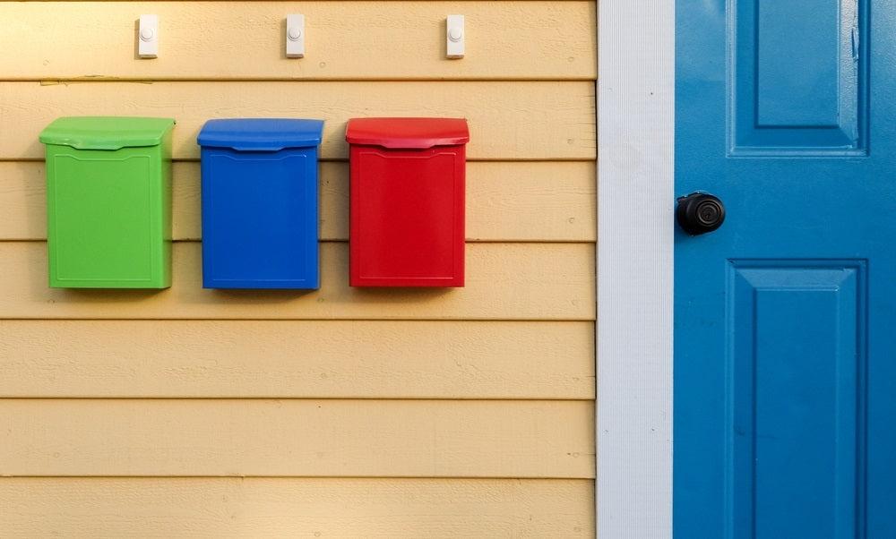 Colorful mailboxes of green, blue, and red on a yellow wooden clapboard