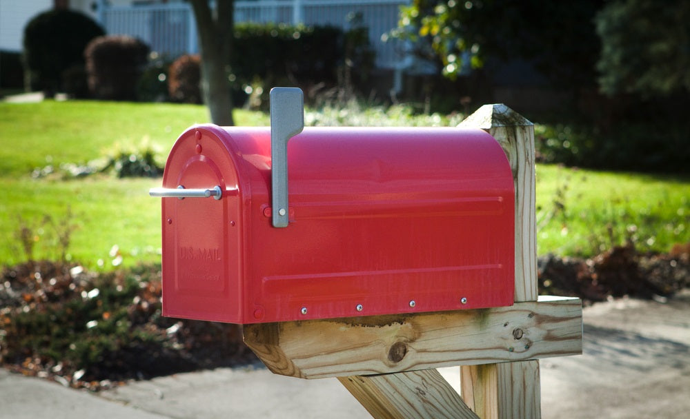 Red rural mailbox on a brown wooden post with silver flag raised close up