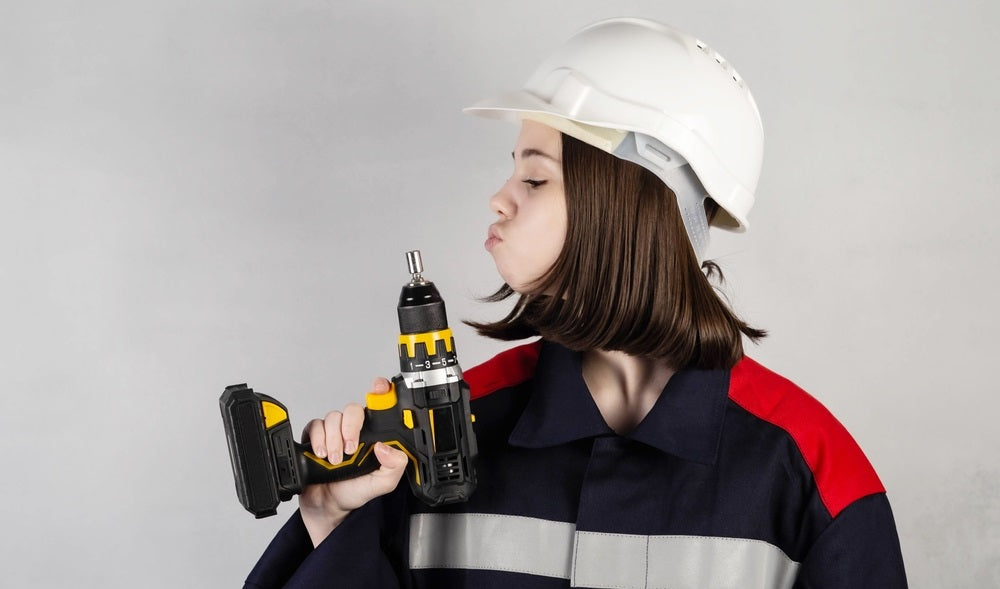 young girl with a drill in her hands, in a construction helmet and overalls