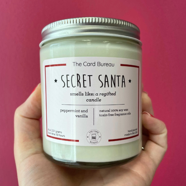 https://cdn.shopify.com/s/files/1/1670/8729/products/the-card-bureau-home-candles-novelty-tcb-candle-secret-santa-8-oz-29151038013509_600x600.png?v=1629044506