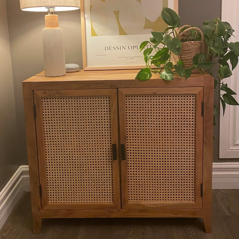 A rectangular wooden buffet with a warm acacia wood finish and woven cane doors. The buffet features two doors with round handles and one fixed shelf for storage. Ideal for adding a touch of bohemian style to your home decor.