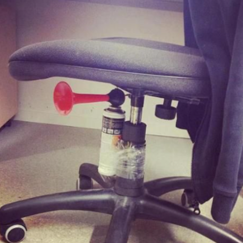 An airhorn is taped securely underneath the seat of an office chair. 