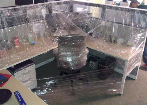 An office cubicle ( full of office equipment) wrapped in plastic wrap. A lot of plastic wrap.