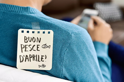 A person wearing an 'April Fools' post-it note with a fish-shaped symbol commonly associated with the holiday, written in Italian, on their back.