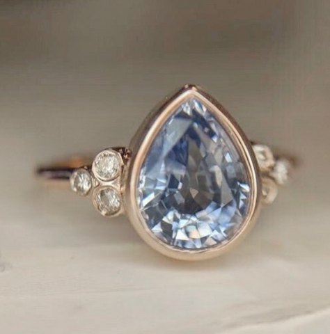 pear shaped pastel blue sapphire bezel set custom engagement rings with three round diamonds on each side