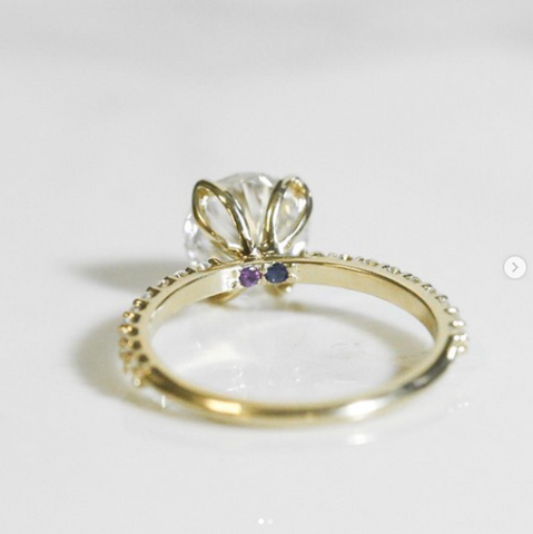 Custom solitaire diamond engagement ring set in yellow gold with two hidden gemstones under the center stone