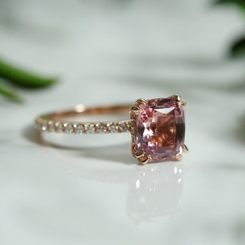 Custom cushion cut pink sapphire and diamond engagement ring set in rose gold with double claw prongs