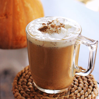 Clear mug with pumpkin spice tea topped with whipped cream, cinnamon, and a pumpkin in the background