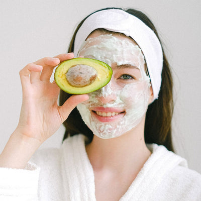 Woman holding half an avocado with a face mask