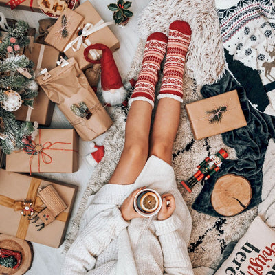 Christmas scene with gifts and cozy blankets around a person holding a cup of tea with an orange slice