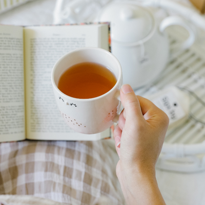 Person holding a cup of mental clarity tea and reading a book