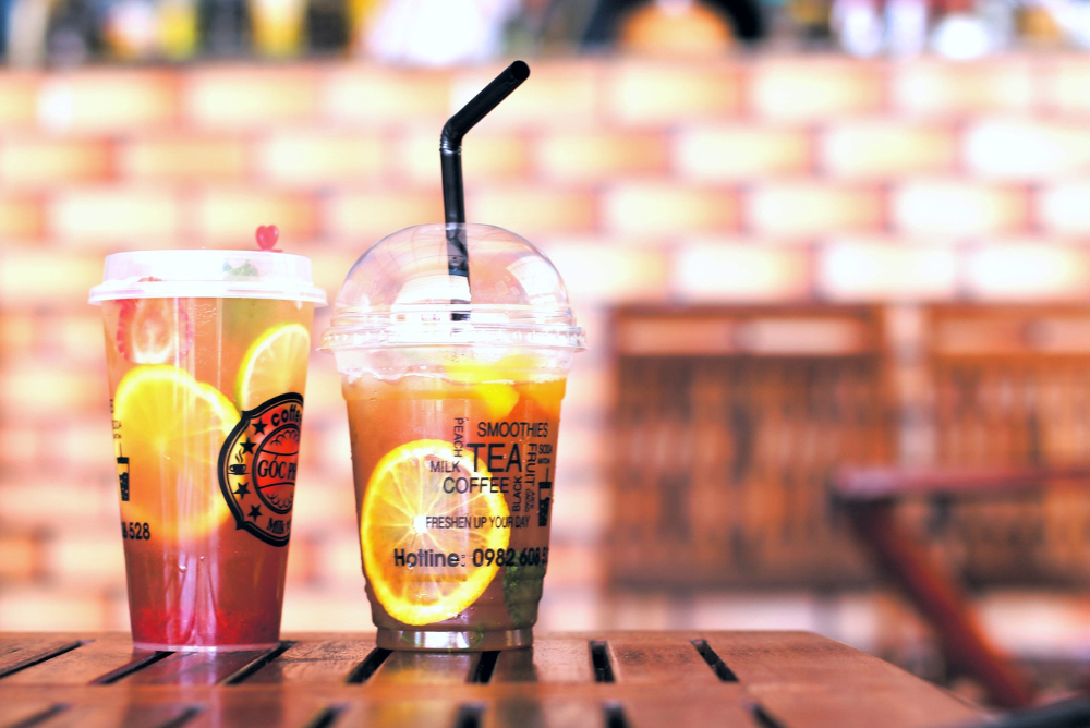 Two glasses of fruity bubble tea on a wooden table next to a windowsill