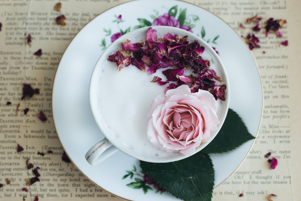 Rose Tea Latte from Sips by recipe in white teacup sprinkled with rose petals sitting on open book