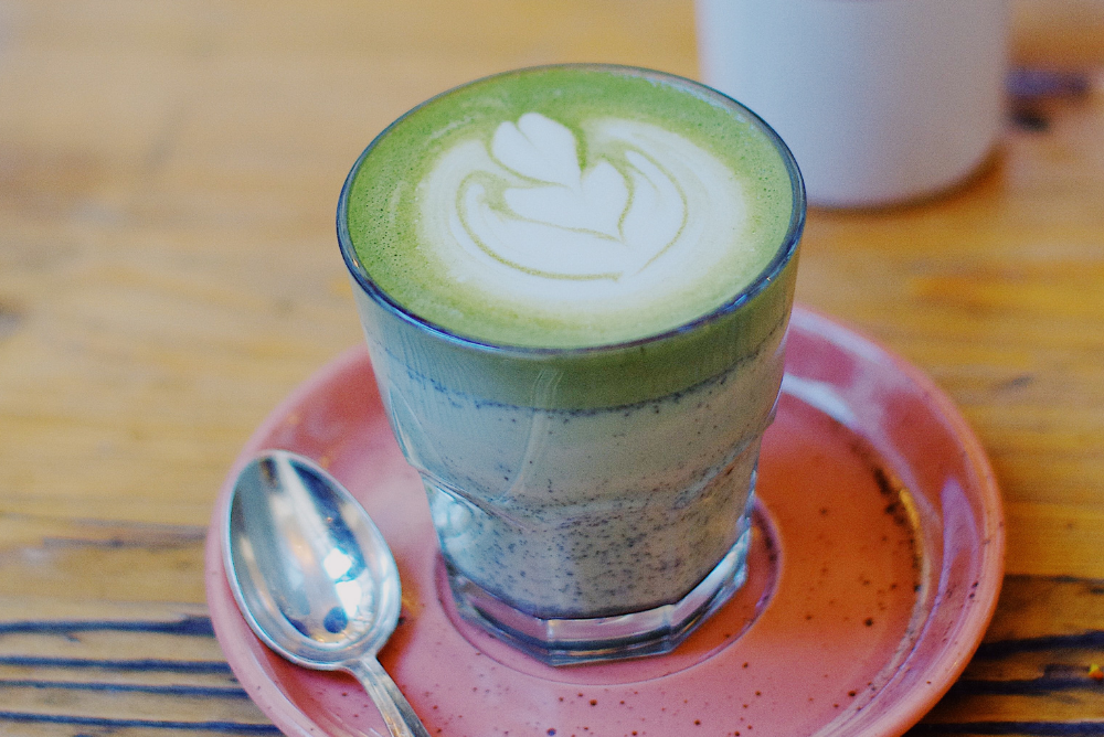 Tokyo Fog green tea matcha latte from Sips by recipe in clear glass on pink saucer with spoon on wood table