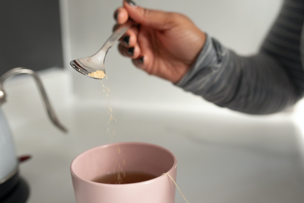 Adding a spoonful of sweetener to a cup of tea in a pink mug