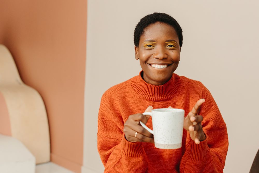 Woman wearing an orange sweater holding a white stoneware mug of tea
