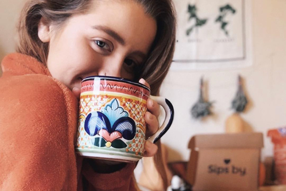 Person in an orange sweater holding a colorful tea mug