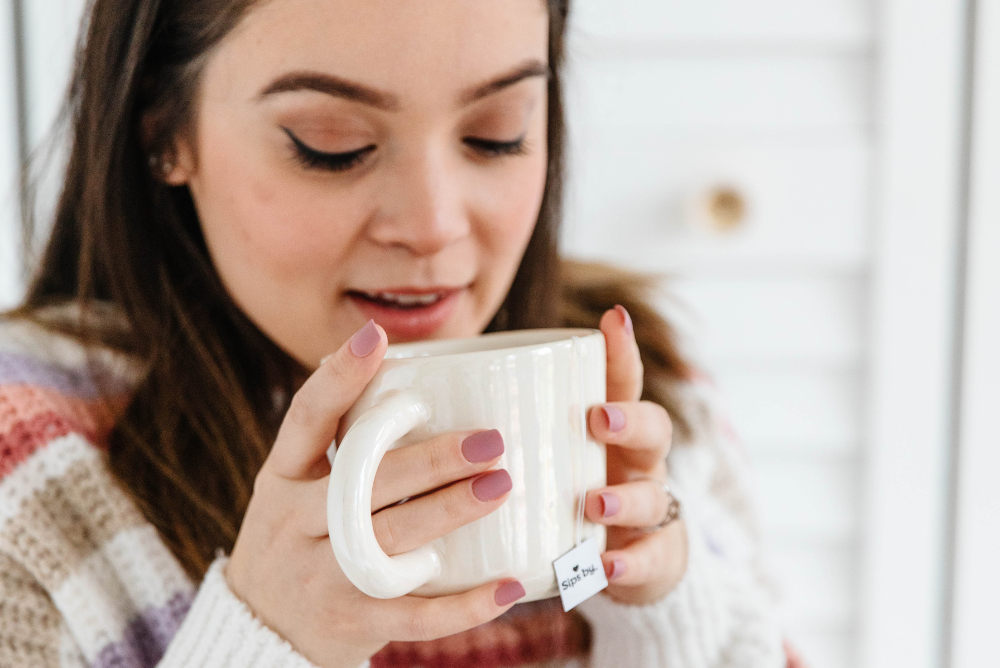 Woman in striped purple and white sweater drinking a cup of tea