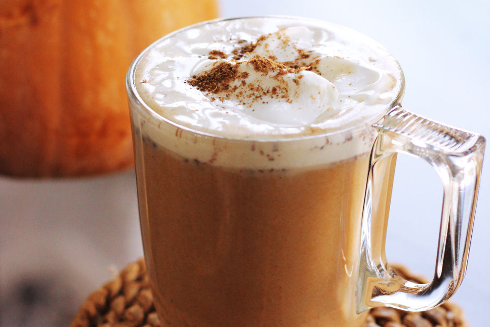 Clear mug with pumpkin spice tea topped with whipped cream, cinnamon, and a pumpkin in the background