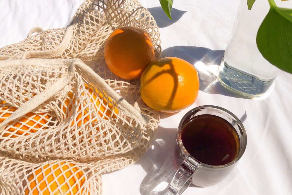 Bag of oranges on a white table with a cup of tea and a pothos plant