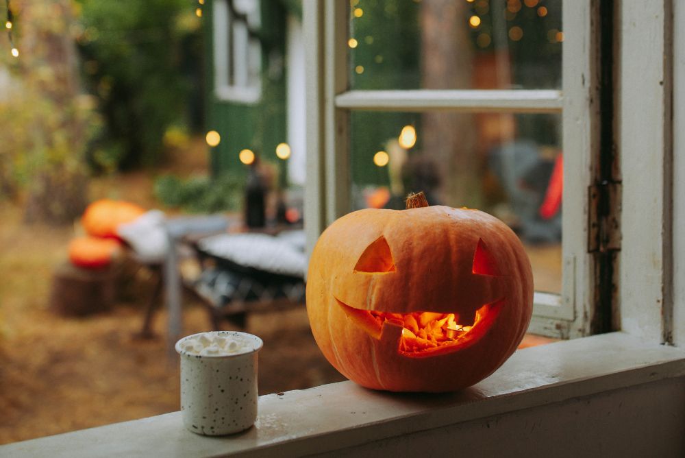 Jack o' lantern and cup of tea on an open windowsill in front of an autumn scene