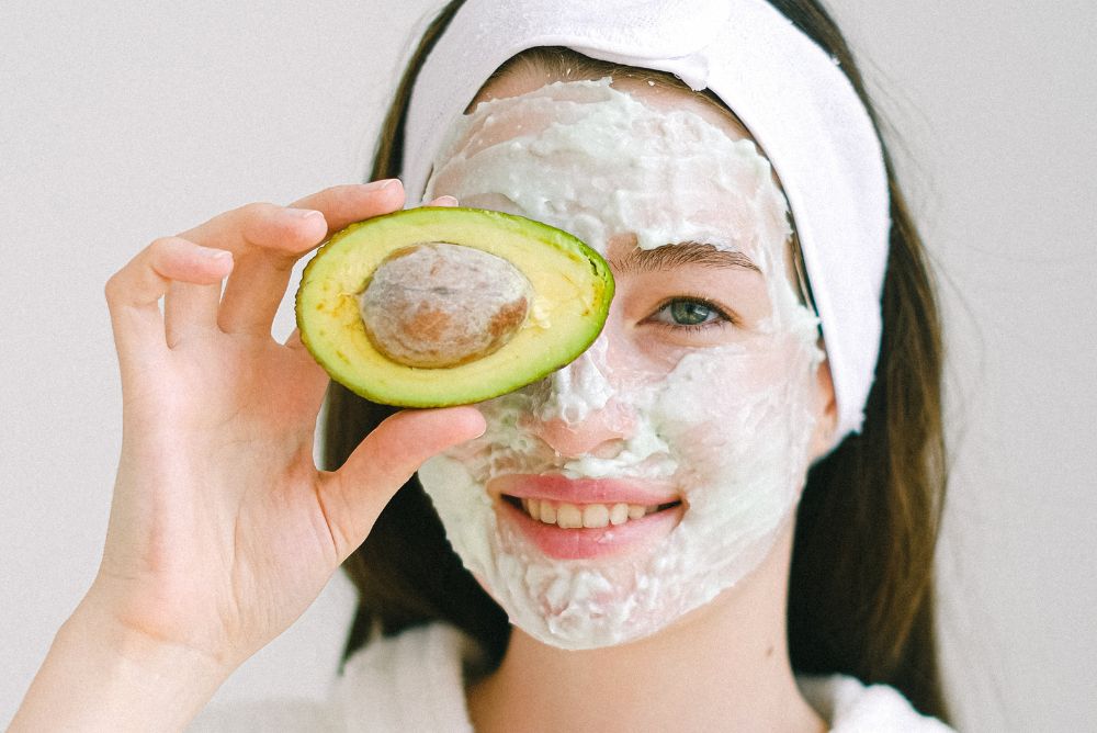Woman holding half an avocado with a face mask