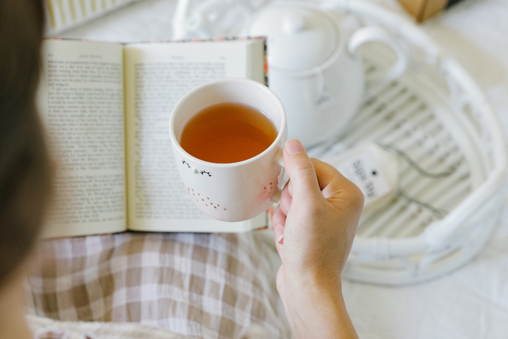 Person holding a cup of mental clarity tea and reading a book