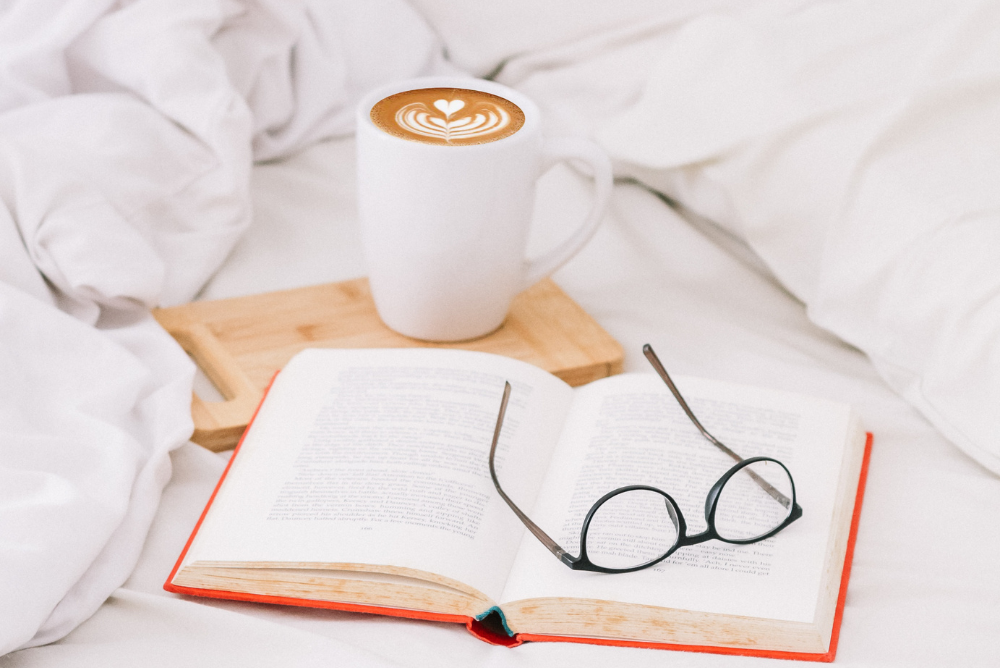 Cup of coffee in bed with an open book and glasses