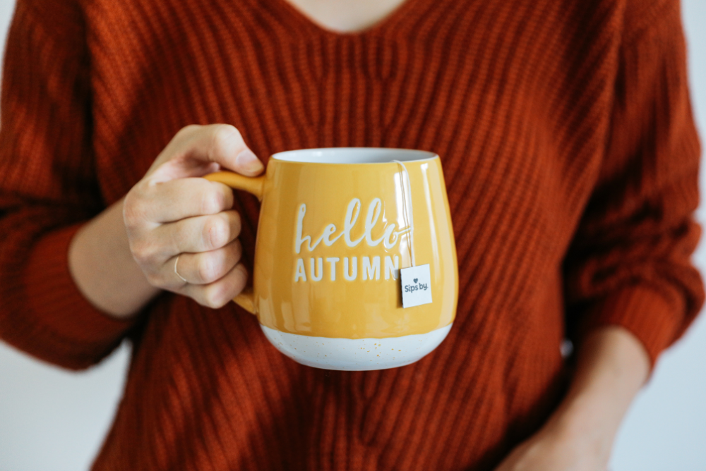 Person holding a yellow hello autumn mug with Sips by teas