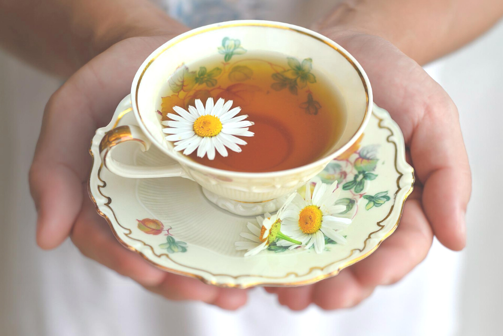 Hands holding a teacup with chamomile tea