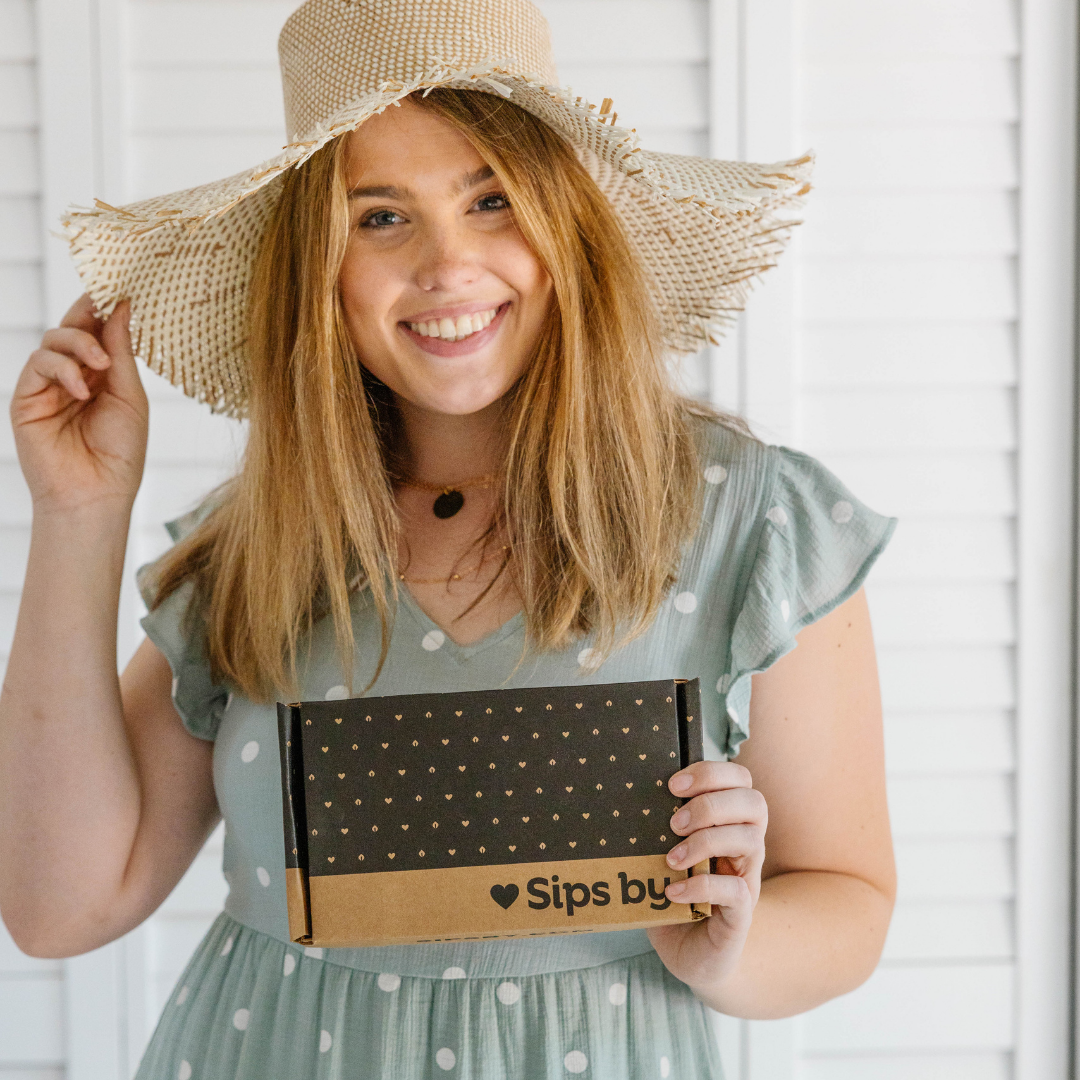 Shop the best happy teas for a mood-boost from Sips by with picture of woman in hat smiling and holding a Sips by tea box