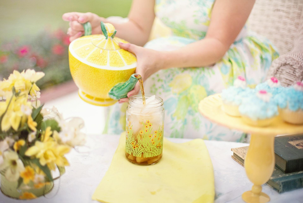 Person pouring a glass of iced tea from a lemon teapot