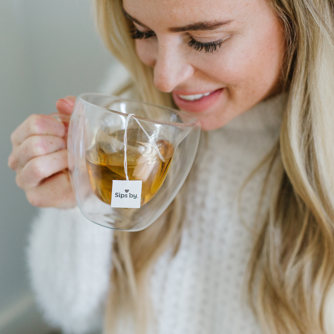Wellness Tea Shop at Sips by woman in white sweater with blond hair drinking tea out of glass heart mug