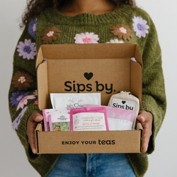 Person in green floral sweater holding an open Sips by Box with chai tea samples