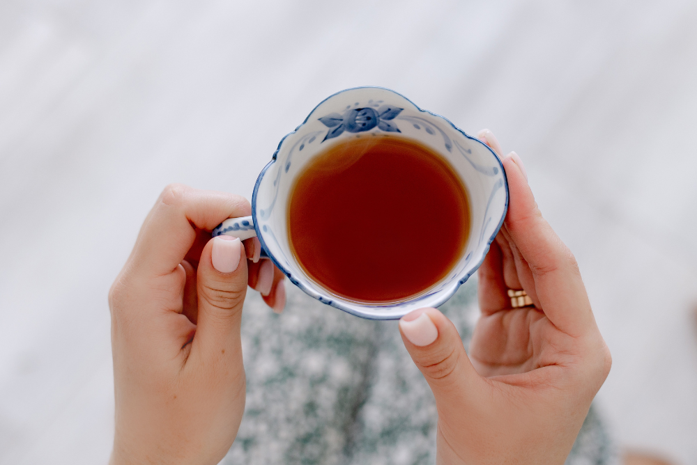 Hands holding a blue floral tea cup with energy tea