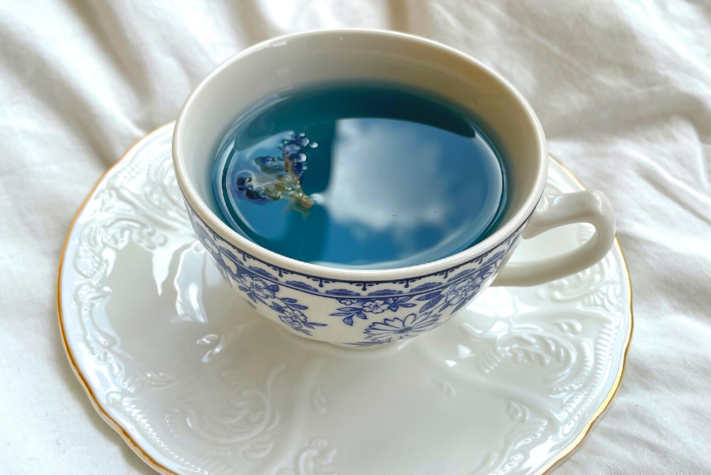 Butterfly pea flower tea in a white teacup with a cloud reflected in the tea