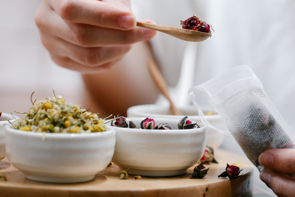Person making herbal tea with empty tea bags, rose petals, and dried chamomile