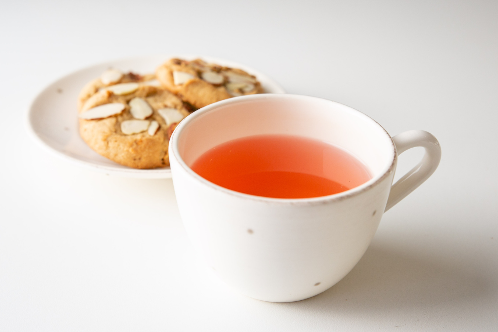 Cup of almond cookie herbal tea with plate of biscuits