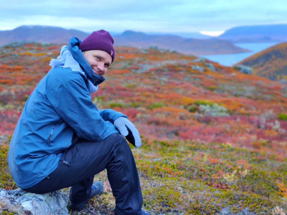 TaikaFlown Sami istuu kivellä ja katselee syksyistä vuoristomaisemaa.