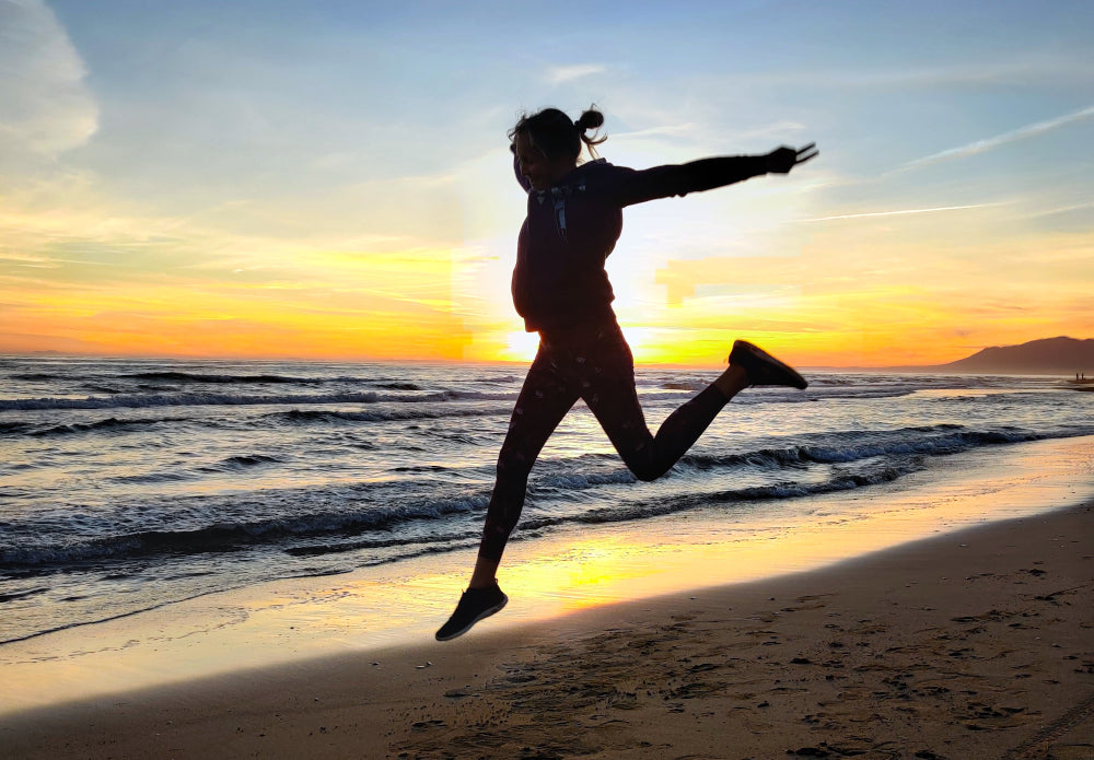 Nainen hyppää rannalla auringonlaskun aikaan.