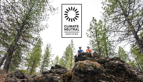 Two people wearing Showers Pass gear sitting atop a rocky ledge, with a climate-neutral certified logo