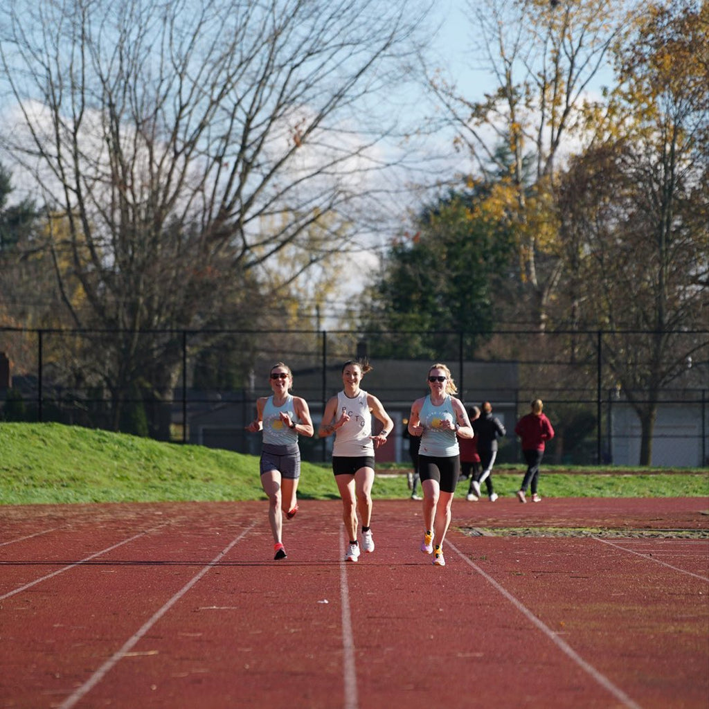 Three Rose City Track Club members jogging side by side on a public outdoor track