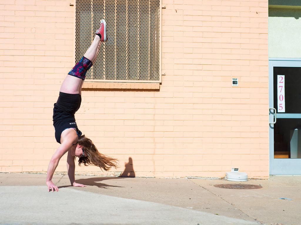 female athlete doing a walking handstand on sidewalk outside