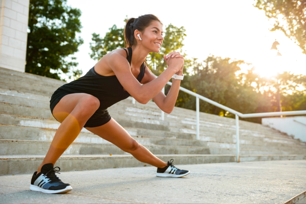 smiling woman wearing earphones and stretching in front of stairs