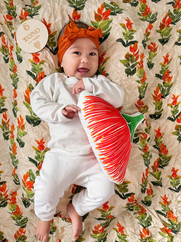 napua 6 months old wearing imi jogger set laying on a ohia lehua swaddle next to a ohia lehua pillow